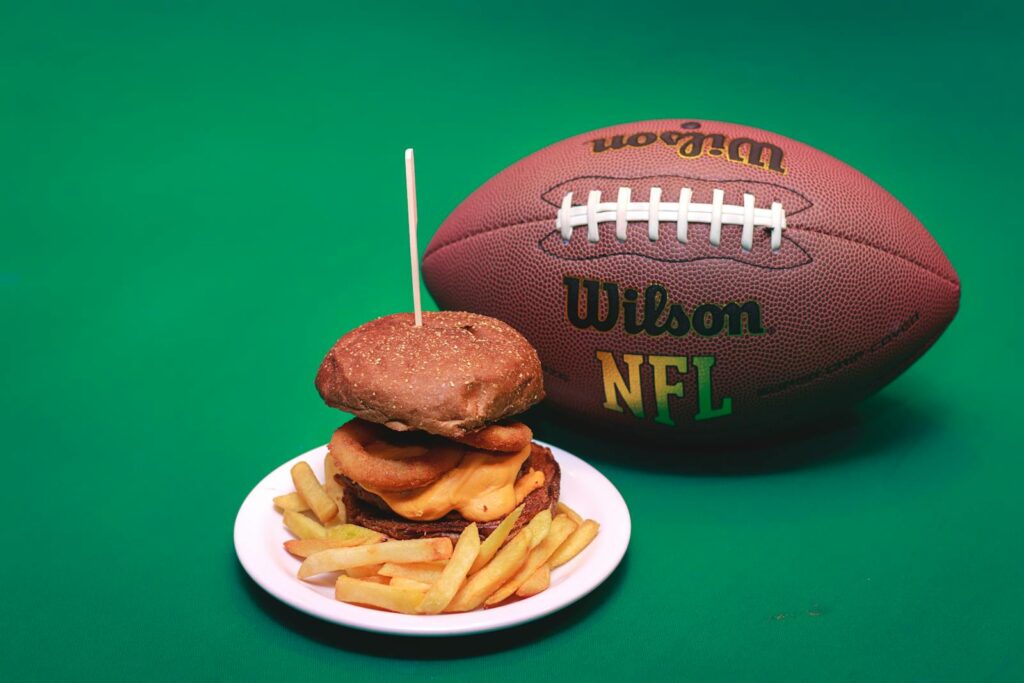 A cheeseburger and fries on a plate with a Wilson NFL football on a green background.